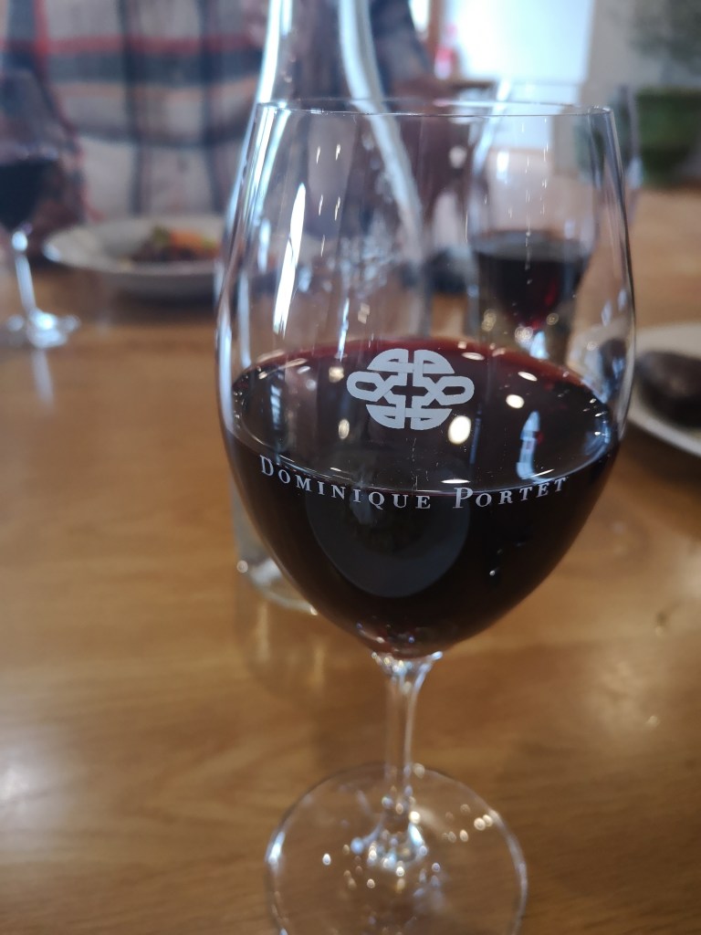 A glass of red wine with the Dominique Portet branding on it