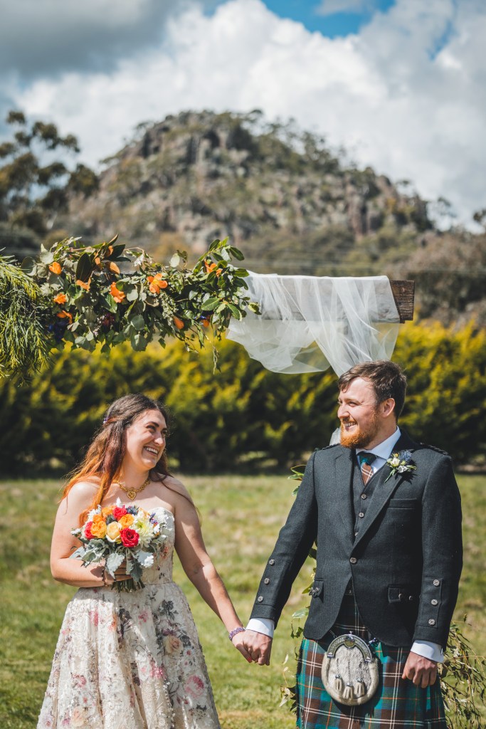 A bridge and groom smile at each other holding hands
