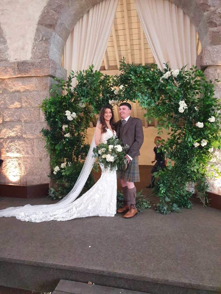 A bridge and groom pose in front of a leafy arch