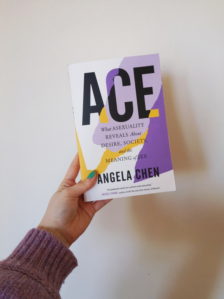 A hand holds up a copy of Ace by Angela Chen, the cover has purple and yellow splodges on it