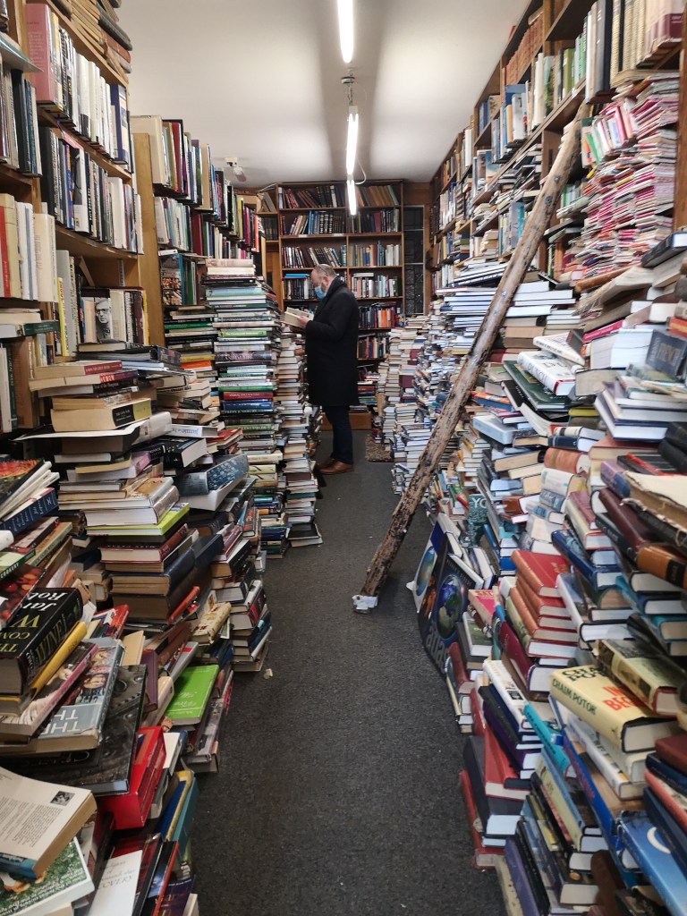 A bookshop with an overwhelming amount of books stacked up on either side of a walkway