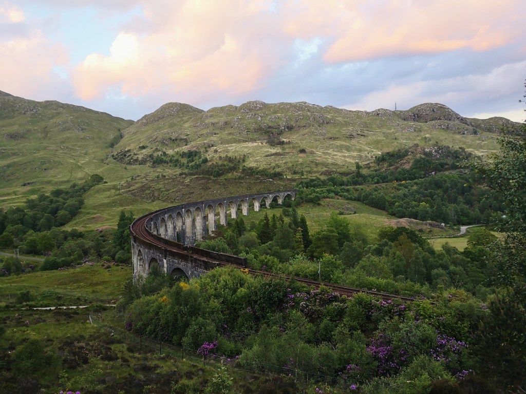 A railway bridge curves through green hills