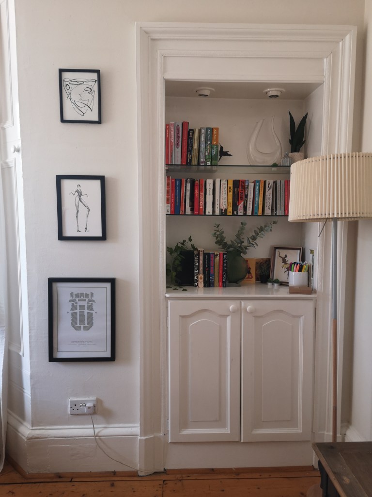 A shot of a little bookshelf which is also decorated with plants and framed art