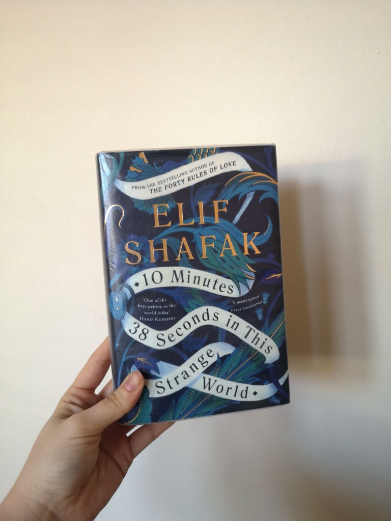 A hand holds up 10 minutes and 38 seconds in this strange world which has a blue patterened cover