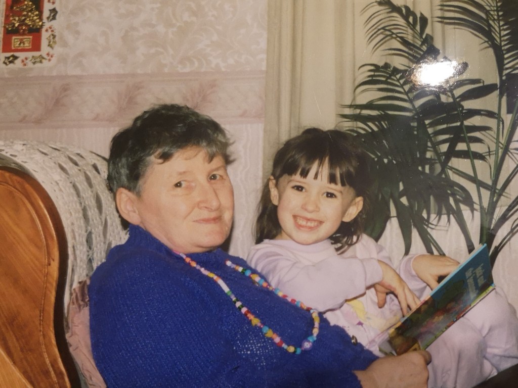 A little baby me sits on my granny's lap as she reads a book to me