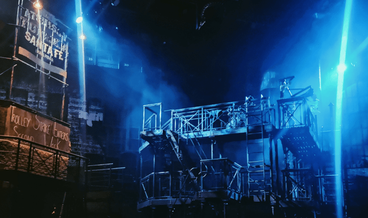 Various platforms and ladders like an American fire escape shine under blue stage lights