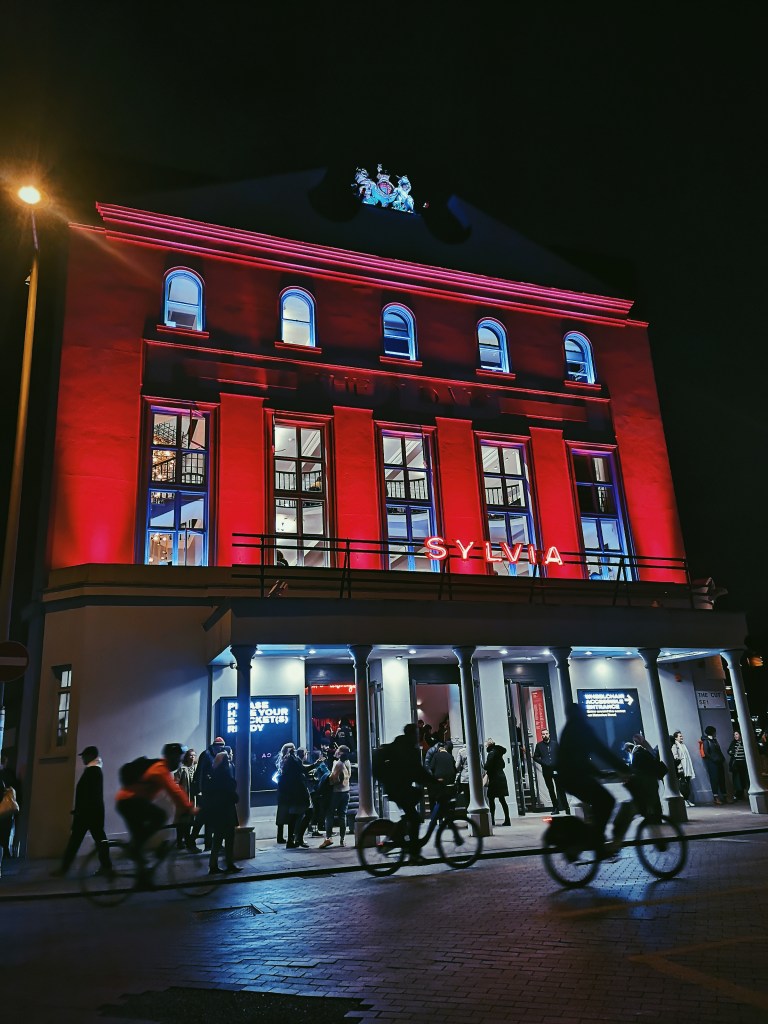 The outside of the Old Vic theatre with red light illuminating the square pillars