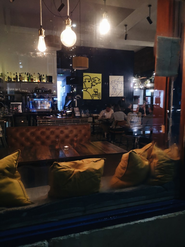 A cosy restaurant with cushions at the window and artwork on the walls