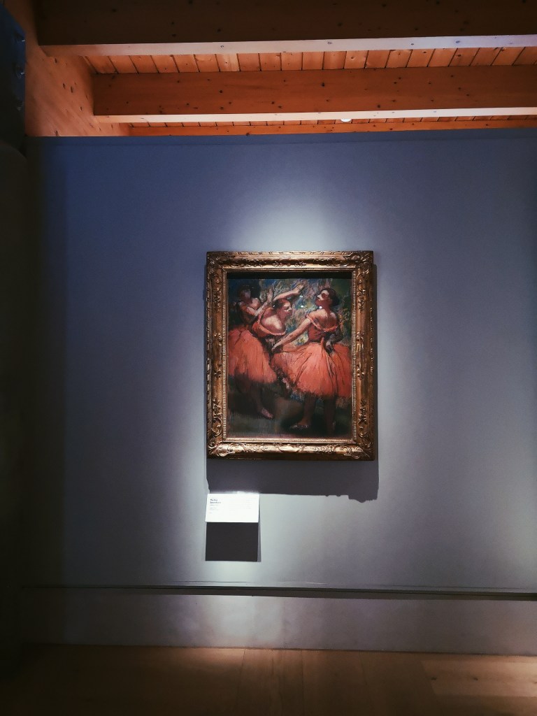 A framed Degas painting on three ballerinas in red skirts