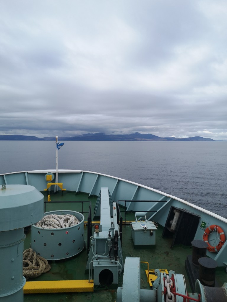 The front of a ferry with the sea, mountains and clouds in the background