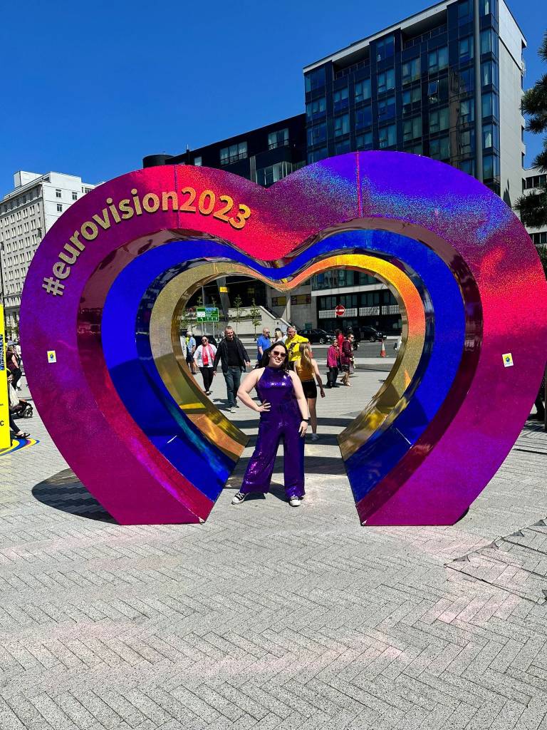 Inside a giant outline of a heart I am posing in my purple sequined jumpsuit