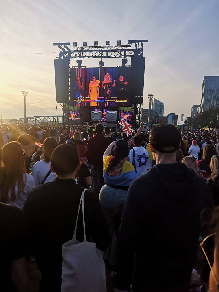 The large screen showing the Eurovision final towers over a large crowd of people standing