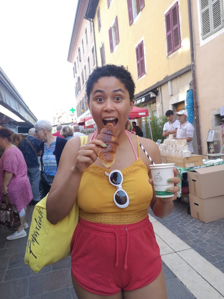 Danielle makes an excited face with an open mouth as she goes to bite her croissant