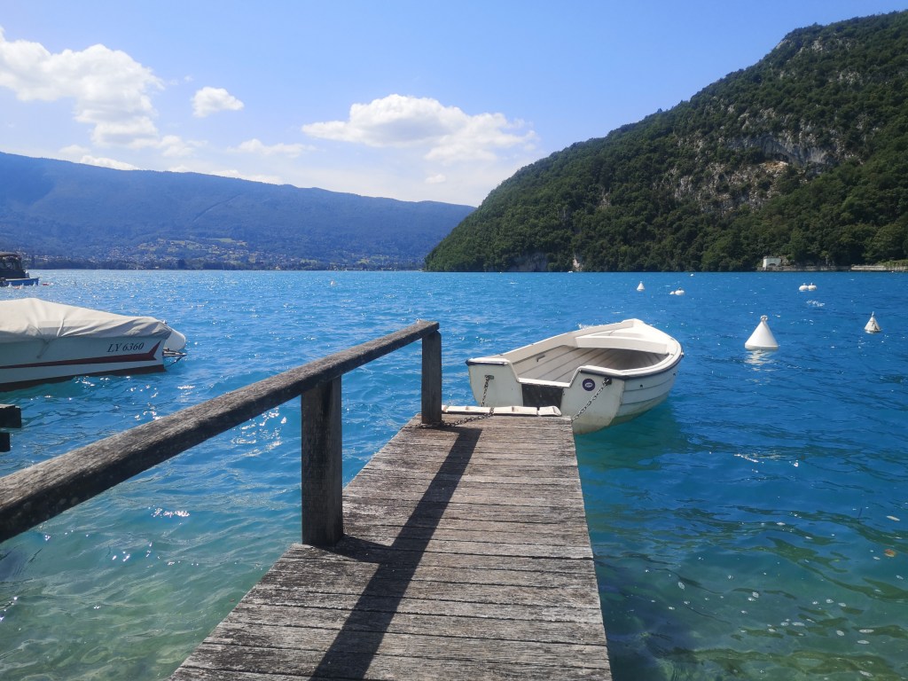 A wee white boat floats at the end of a wooden dock