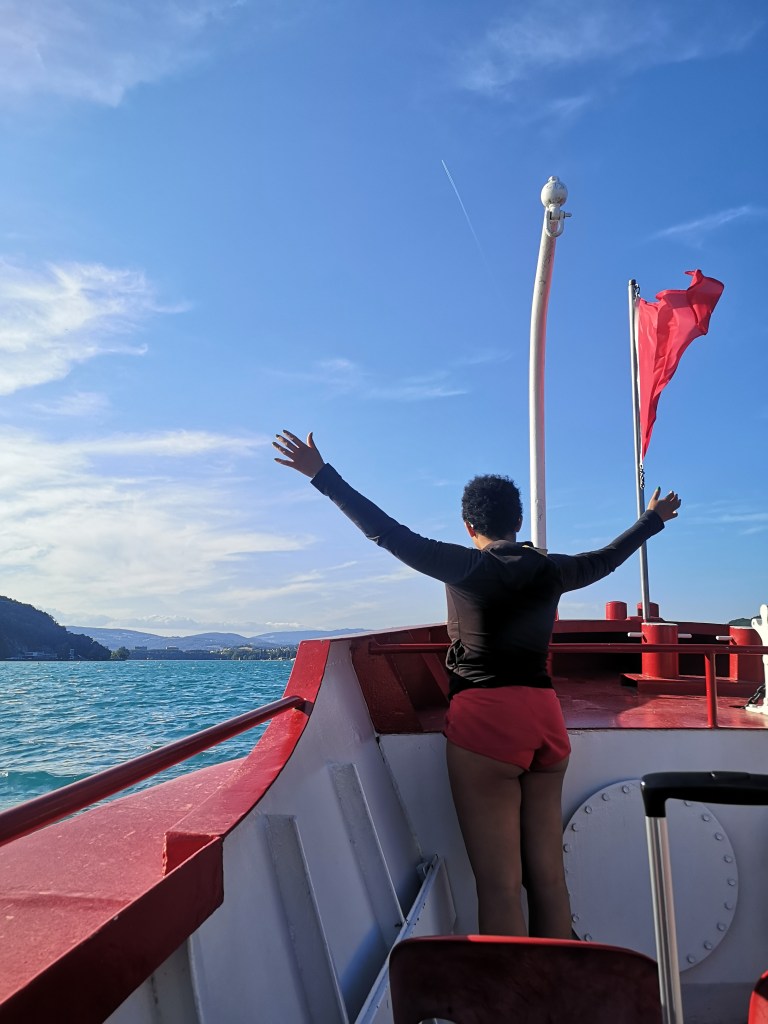 Danielle stands with her arms stretched out on a boat overlooking the water