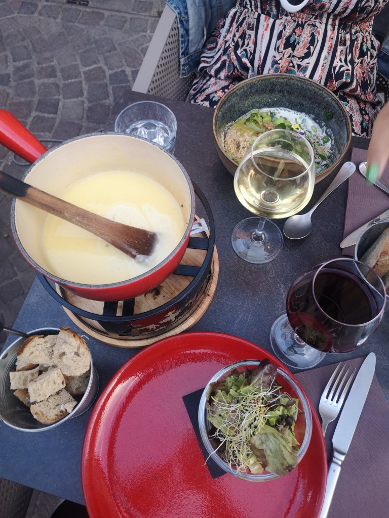 An overhead shot of a dinner table with a cheese fondue pot and glasses of wine