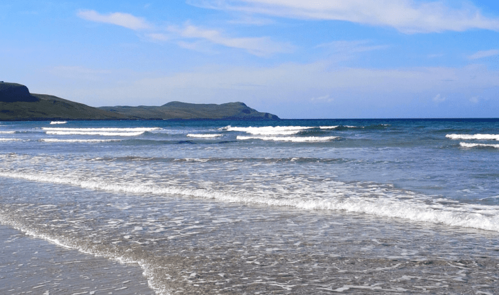 Waves rolling in towards a beach with hills in the background
