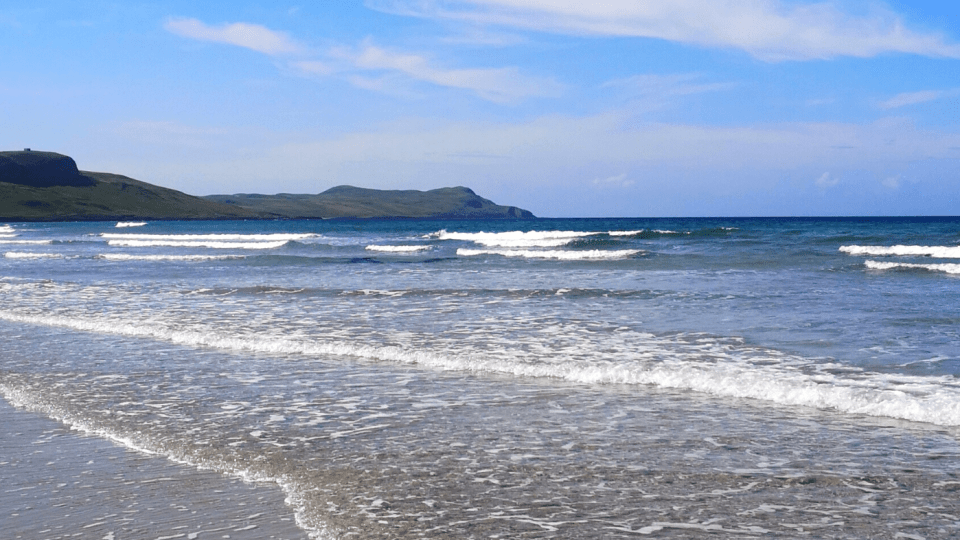 Waves rolling in towards a beach with hills in the background