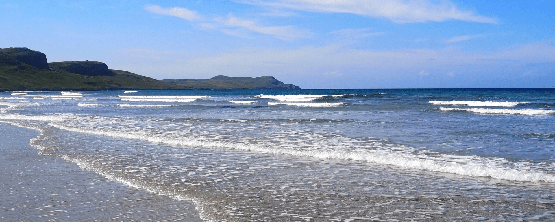 Waves rolling in towards a beach with hills in the background