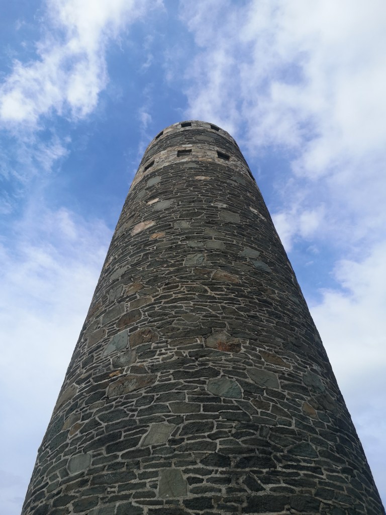 An upward shot of a tall stone tower against a blue and cloudy sky