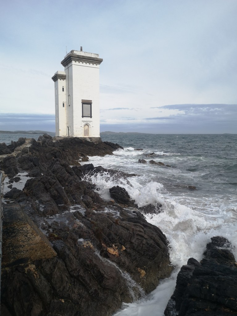 A rectangular white lighthouse surrounded by the sea
