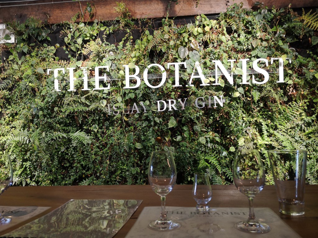 A leafy wall with a sign saying The Botanist and some glasses on a table