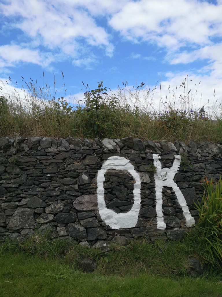 'Ok' is written in white paint on a stone wall surrounded by grass.