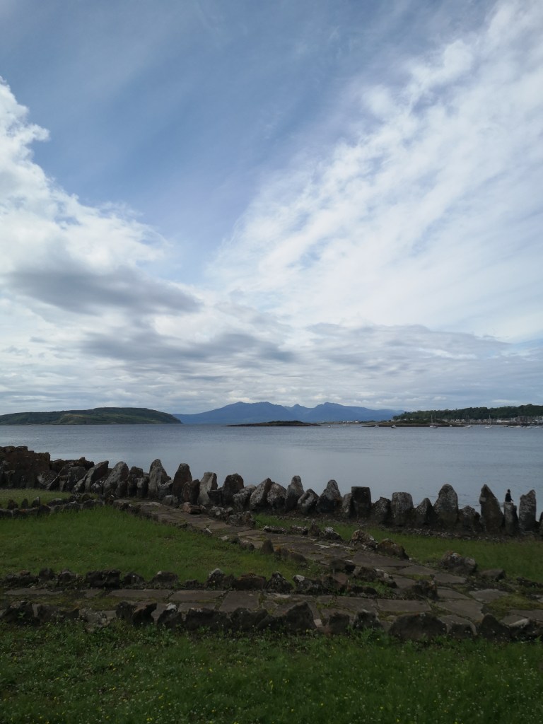 Mountains in the distance across the sea and rocks lining the grass in the foreground