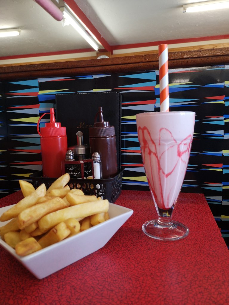 A strawberry milkshake and a bowl of chips on a diner table