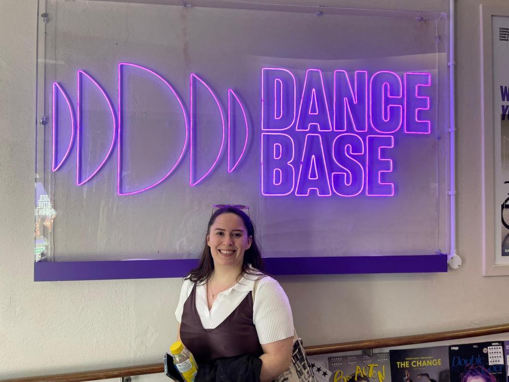 I smile and stand in front of the Dance Base neon sign