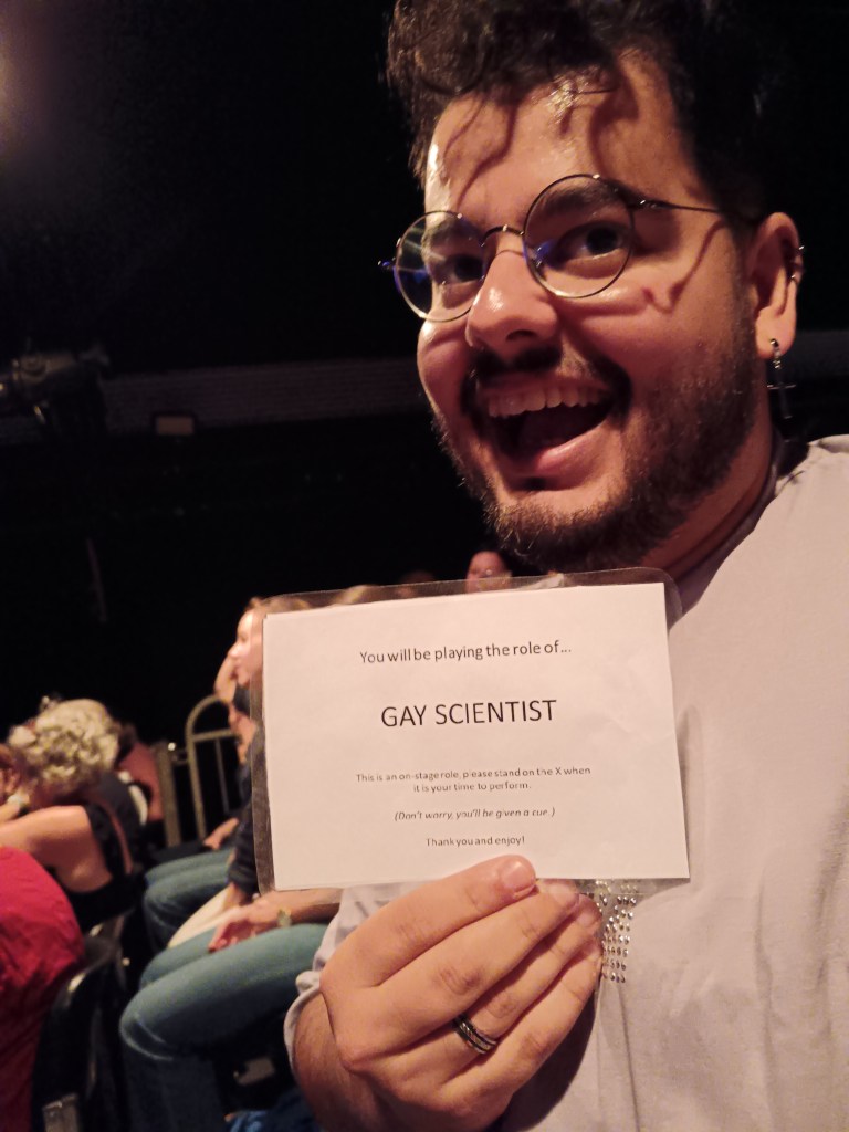 Bruno smiles holding up a sign that says Gay Scientist