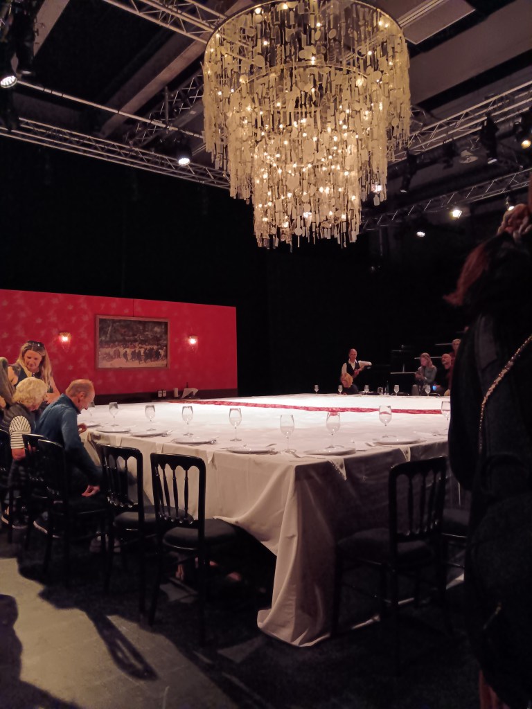 A large dinner table with a big chandelier hanging made out of recycled plastic