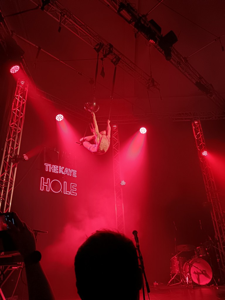 A trapeze artist hangs from the ceiling while kicking their legs back over their head