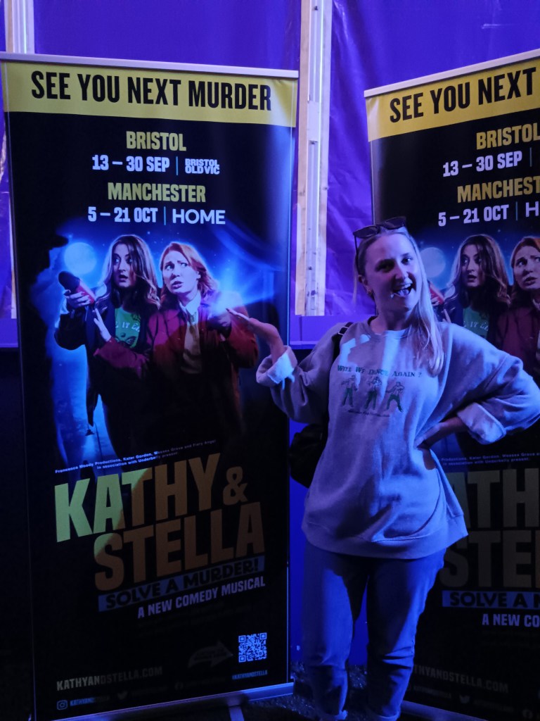 Nathalie smiles and stands with a poster for the show