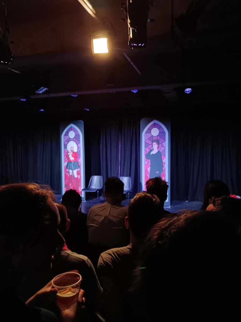 Two bits of set depicting drag queens in the style of stain glass windows stand on stage