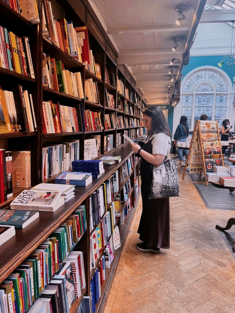 I stand beside a long bookshelf reading a blurb