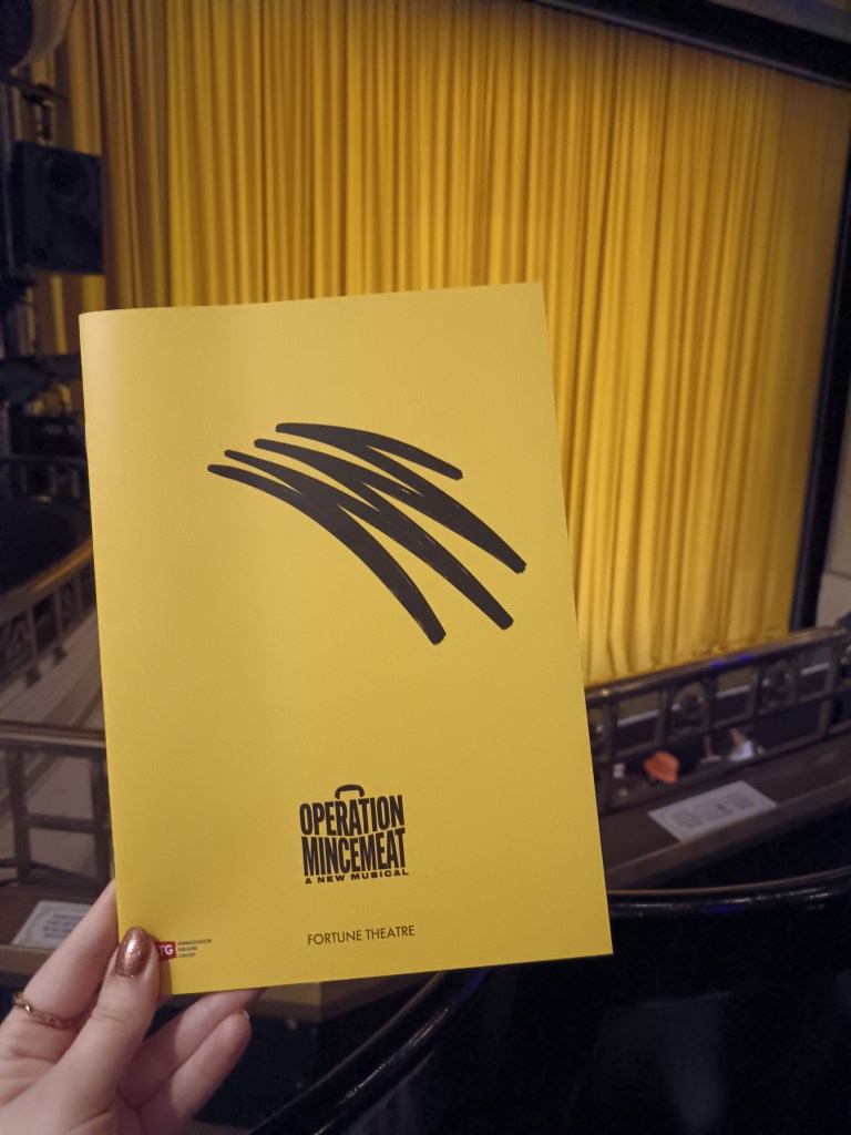 Holding the Operation Mincemeat programme up against their yellow curtain