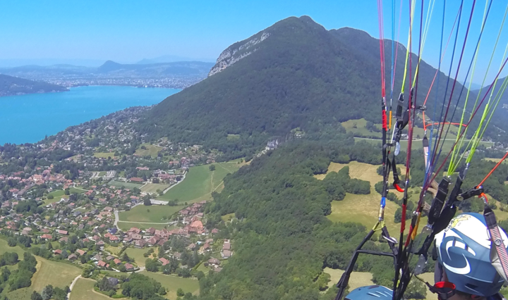 Overhead view of a mountain and blue lake. Paraglider wires cross over one side