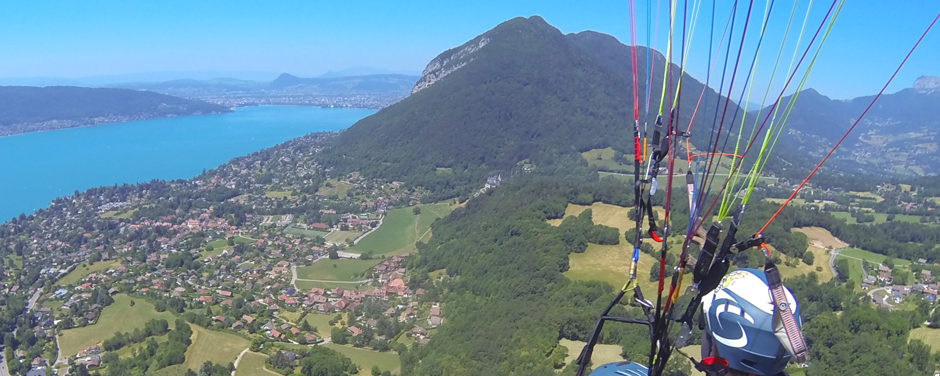 Overhead view of a mountain and blue lake. Paraglider wires cross over one side