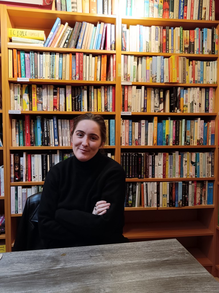 Claire crosses her arms and smiles sitting in front of a bookshelf