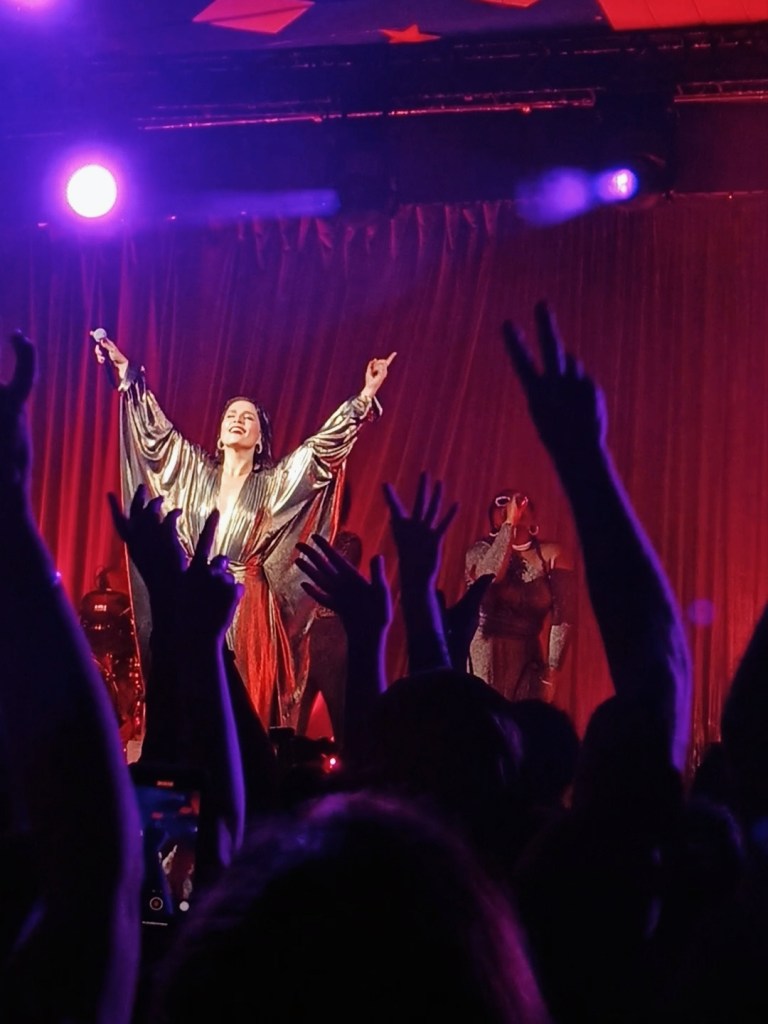 Jessie Ware holds her hands in the air looking out to the crowd