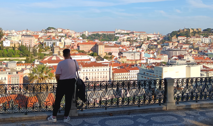 A man stands by a railing looking out over a city shining in the sun