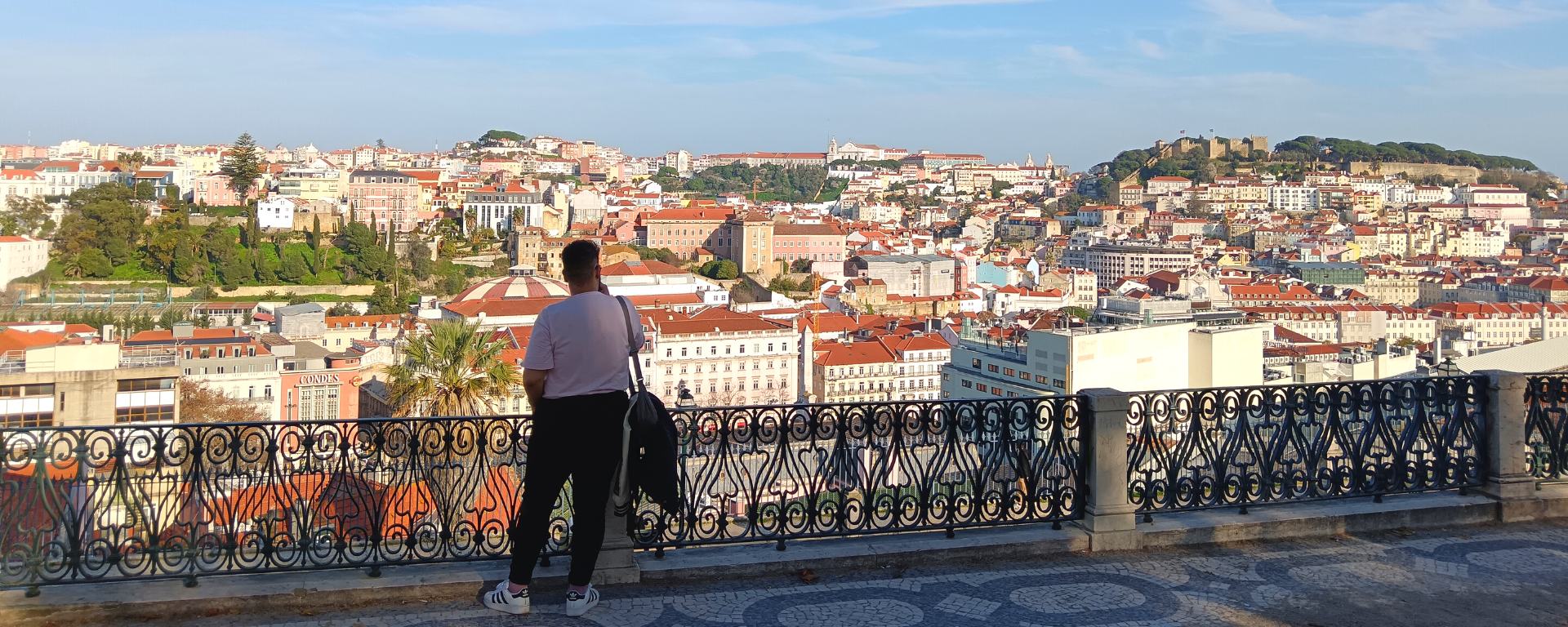 A man stands by a railing looking out over a city shining in the sun