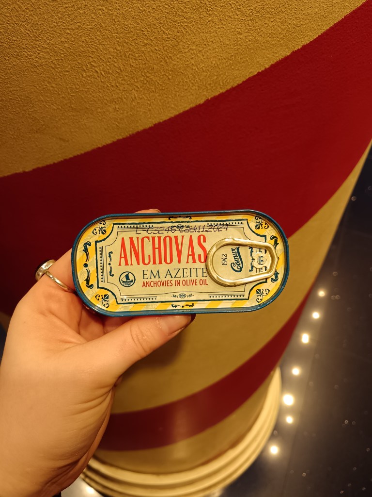 An adorable tin of anchovies held in front of a candle striped pillar