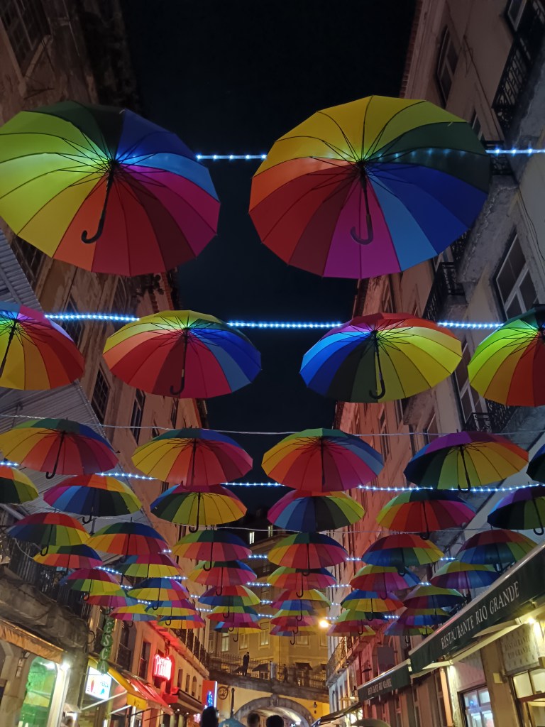 Rows of rainbow umbrellas hand over a street of bars
