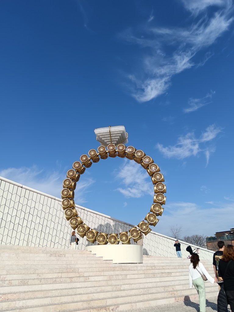 A sculture of a diamond ring shines against the blue sky