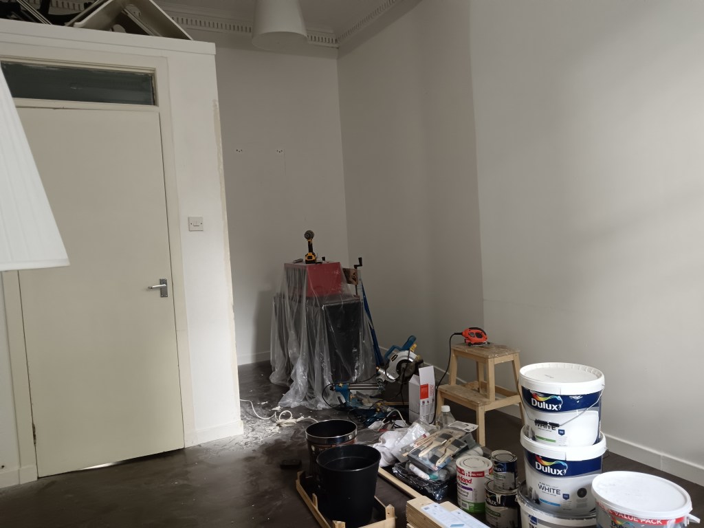 A plain white room with piles of DIY materials on the floor in the middle of the room