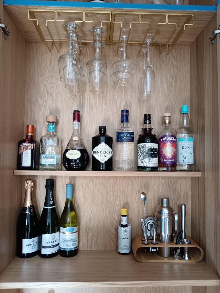 A drinks cabinet with wine and cocktail glasses hanging from the stems