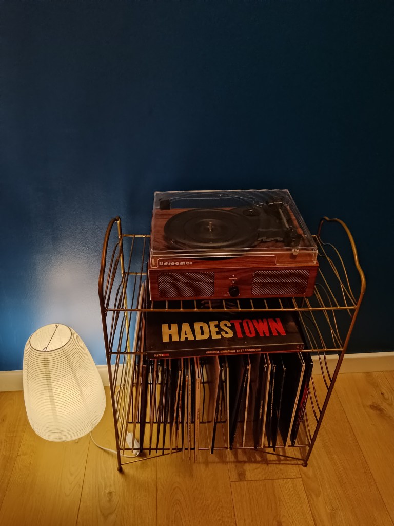 A record player on a gold rack and a paper lantern floor lamp