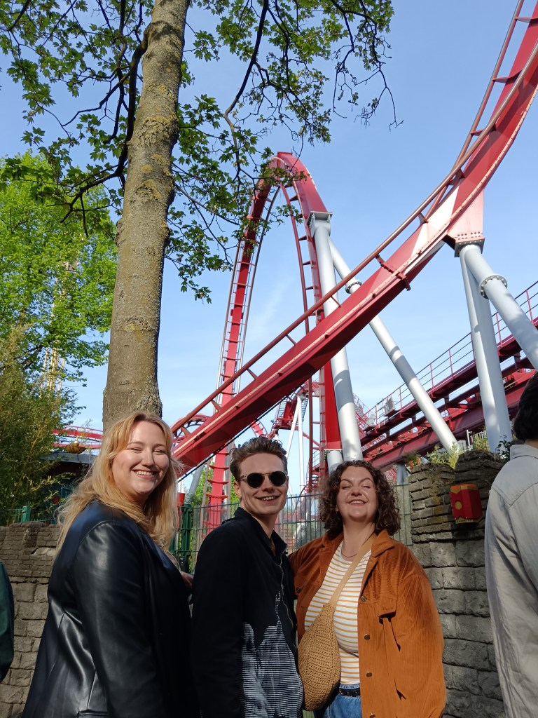 Hanna, Jack and Laura smile in front of a big rollercoaster